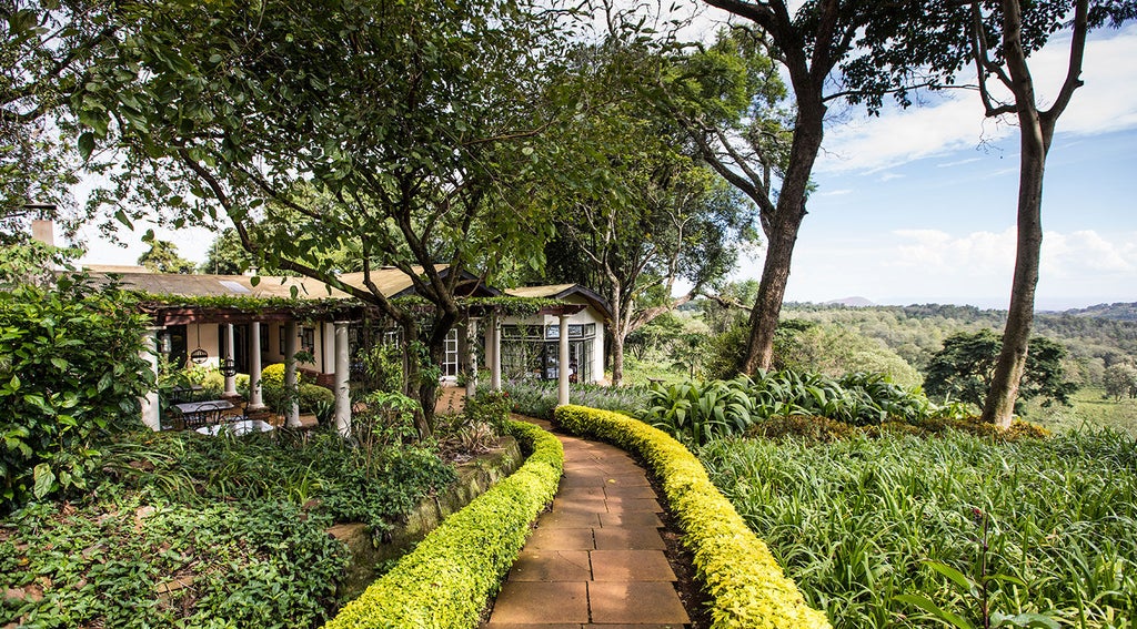 Traditional Tanzanian luxury lodge with thatched roof cottage nestled among lush gardens, overlooking misty green hills at sunset