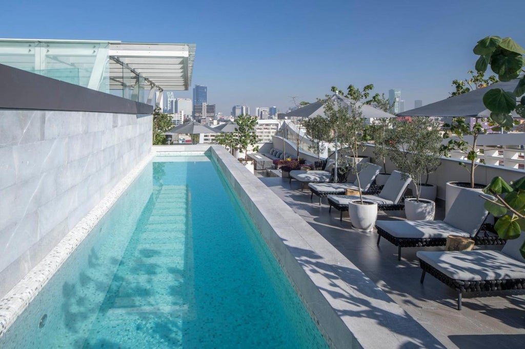 Modern luxury hotel building with white geometric facade, floor-to-ceiling windows, and tropical landscaping at twilight in Mexico City