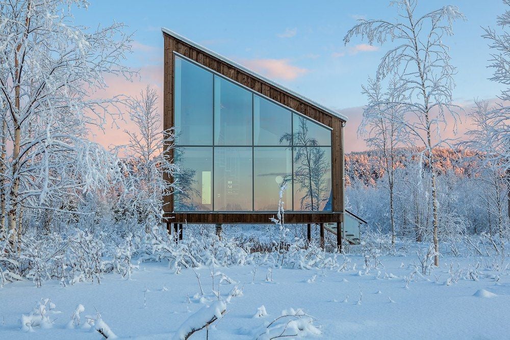 Minimalist wooden cabin suite with large windows overlooking snowy landscape, featuring modern Nordic design and luxurious natural elements at Arctic Bath hotel