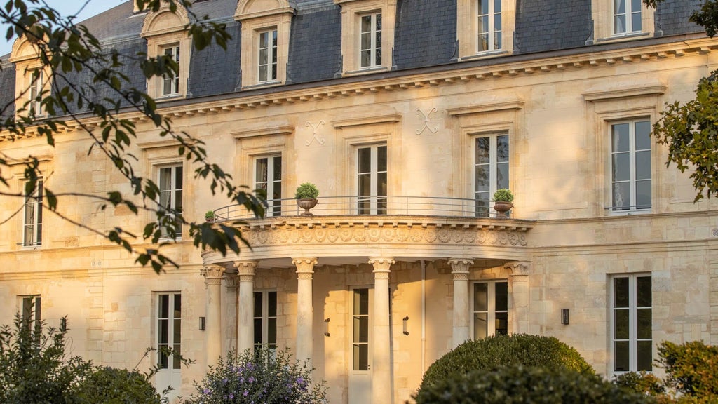 Elegant French luxury hotel nestled in vineyard landscape, featuring stone facade, manicured gardens, and warm golden sunset lighting