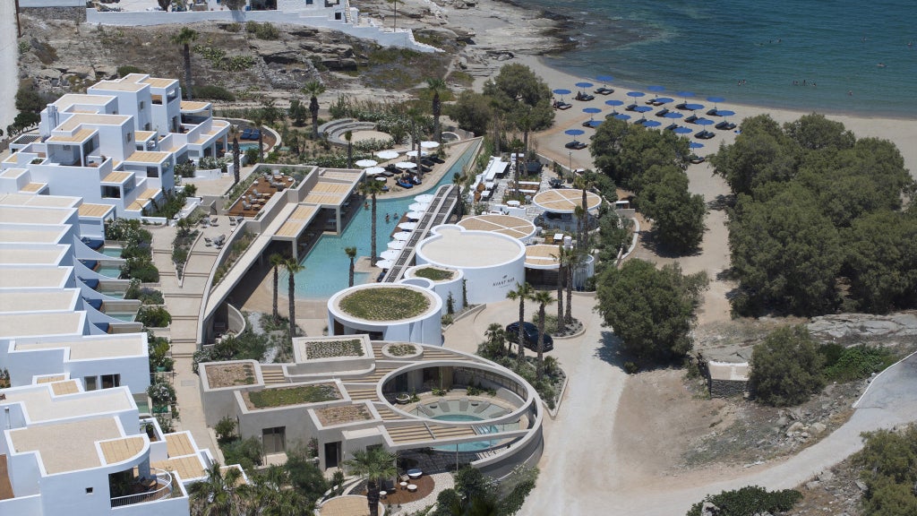 Modern white hotel with infinity pool overlooking bright blue Mediterranean Sea, private balconies and stone terrace in Santorini