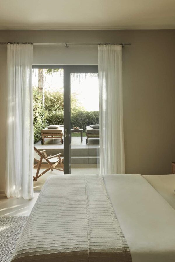 Elegant Greek hotel room with soft white linens, minimalist decor, natural wood accents, and garden view showcasing serene Kefalonian hospitality