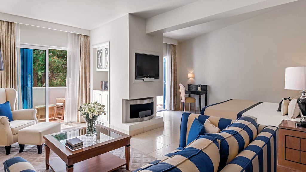 Elegant suite bedroom with king bed, white linens, cream walls, floor-to-ceiling windows overlooking Portuguese coastal gardens