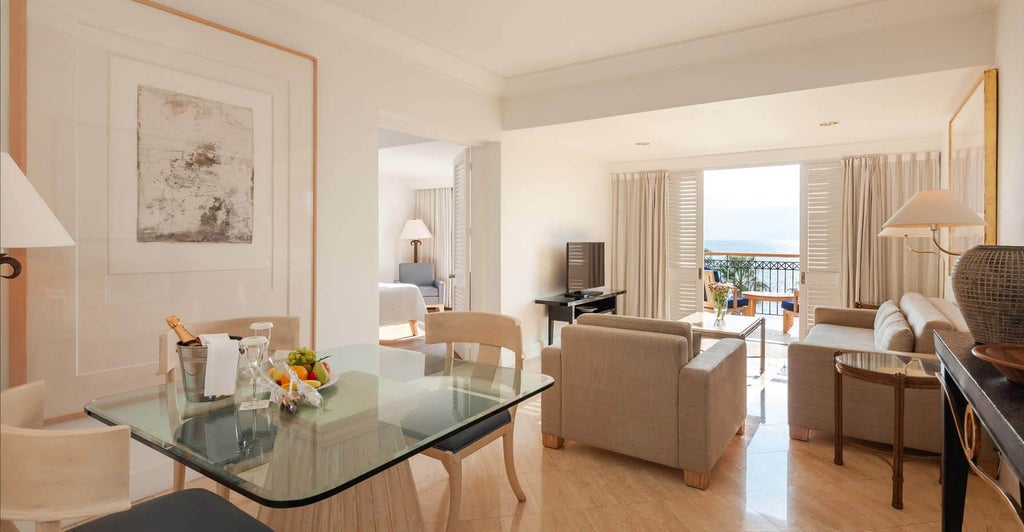 Spacious deluxe suite with modern furnishings, king bed, elegant marble bathroom, and panoramic Mediterranean coastal views from private balcony in Cyprus.