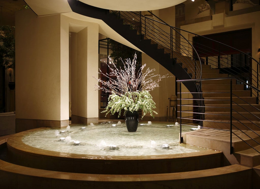 Modern Japanese luxury hotel exterior with glass facade, illuminated signage, and grand circular driveway lined with manicured gardens