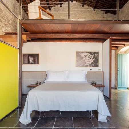 Elegant boutique hotel room with rustic stone walls, minimalist wooden furniture, and soft natural light creating a serene Sicilian countryside atmosphere