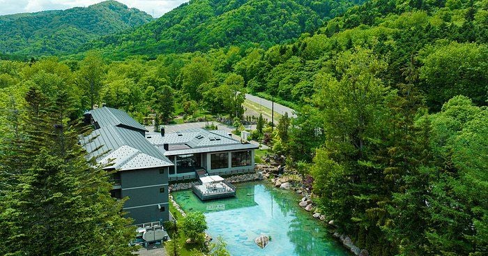 Traditional Japanese luxury hotel with manicured zen garden, wooden walkways, and stone lanterns against serene mountain backdrop