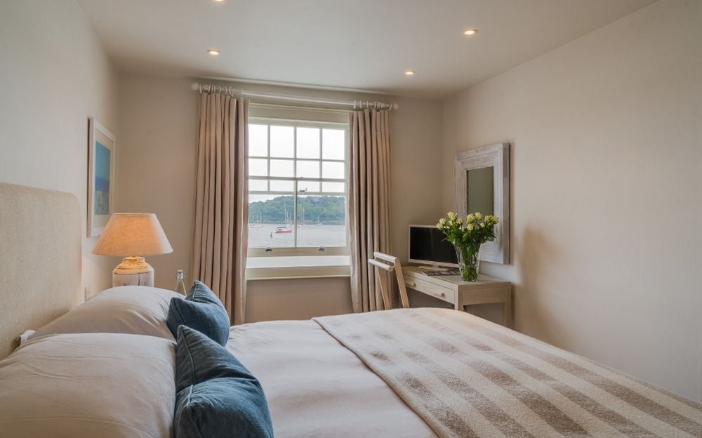 Elegant seaview hotel room with panoramic coastal views, crisp white linens, nautical blue accents, and expansive windows overlooking azure waters of Cornwall.