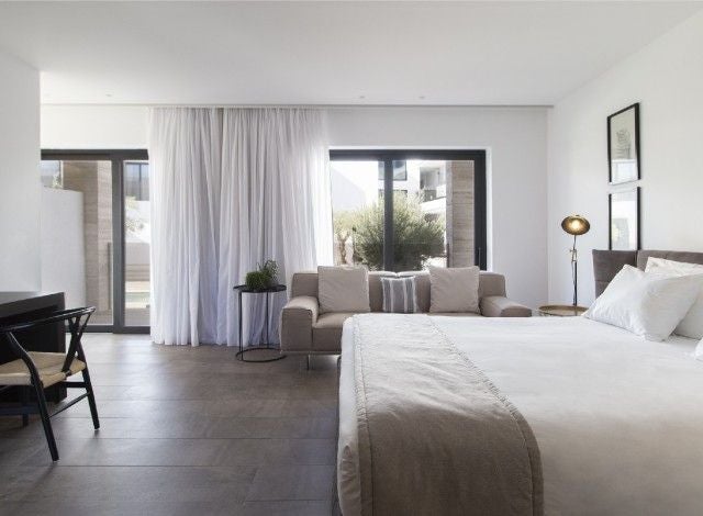 Elegant modern deluxe suite with minimalist white decor, panoramic sea view, sleek designer furniture, and soft natural lighting in Greek island hotel