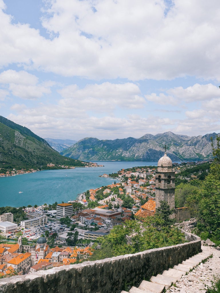 Elegant white sailboat gliding through azure waters of Kotor Bay, with dramatic limestone cliffs and historic Montenegrin coastline in background