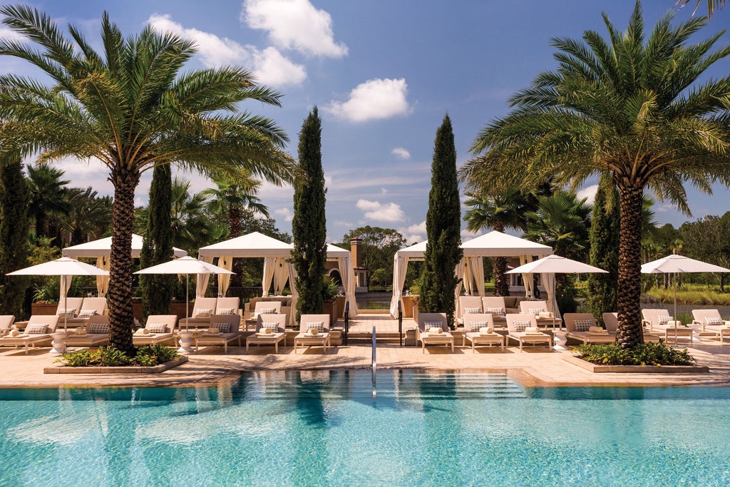 Elegant five-star resort with Spanish-inspired architecture, palm-lined entrance, white facade, and luxurious landscaping under Florida sky