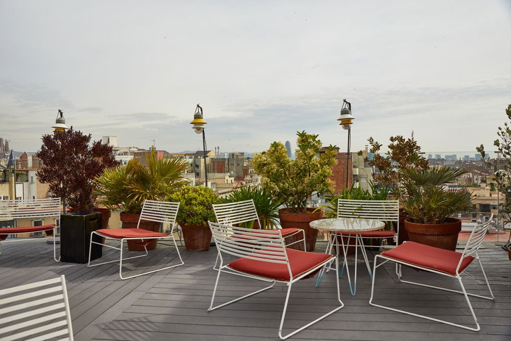 Modern rooftop terrace with infinity pool overlooking Barcelona's cityscape, featuring sleek loungers and panoramic Gothic Quarter views