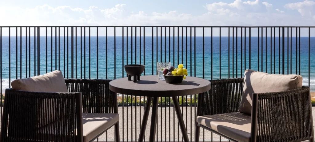 Luxurious Sapphire Junior Suite with elegant white decor, blue accents, plush king bed, and expansive balcony overlooking scenic Corfu landscape