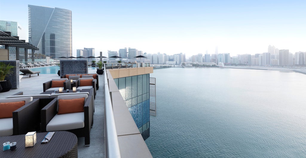 Modern glass skyscraper hotel overlooking Arabian Gulf with infinity pool, private beach, and waterfront promenade at sunset hour