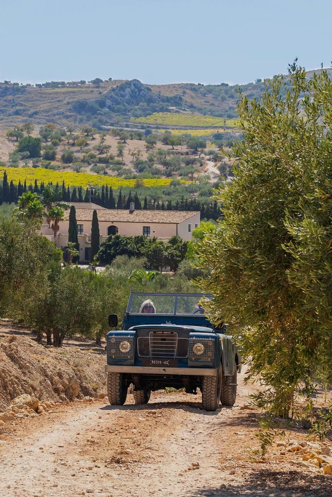 Elegant Sicilian boutique hotel nestled among golden wheat fields, with rustic stone walls and vibrant blue shutters under warm Mediterranean sunlight