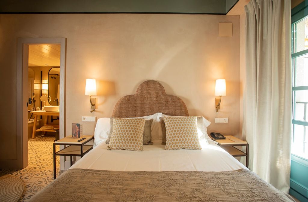 Elegant white-walled Spanish colonial suite with wooden furniture, soft natural light, and refined minimalist decor in Seville hotel room