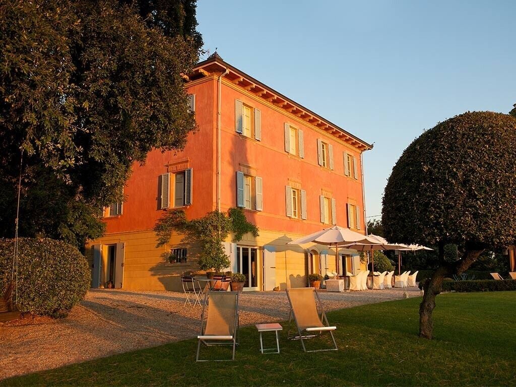 Luxurious boutique hotel nestled in scenic Italian countryside, stone facade with terracotta roof, surrounded by rolling hills and cypress trees at golden hour