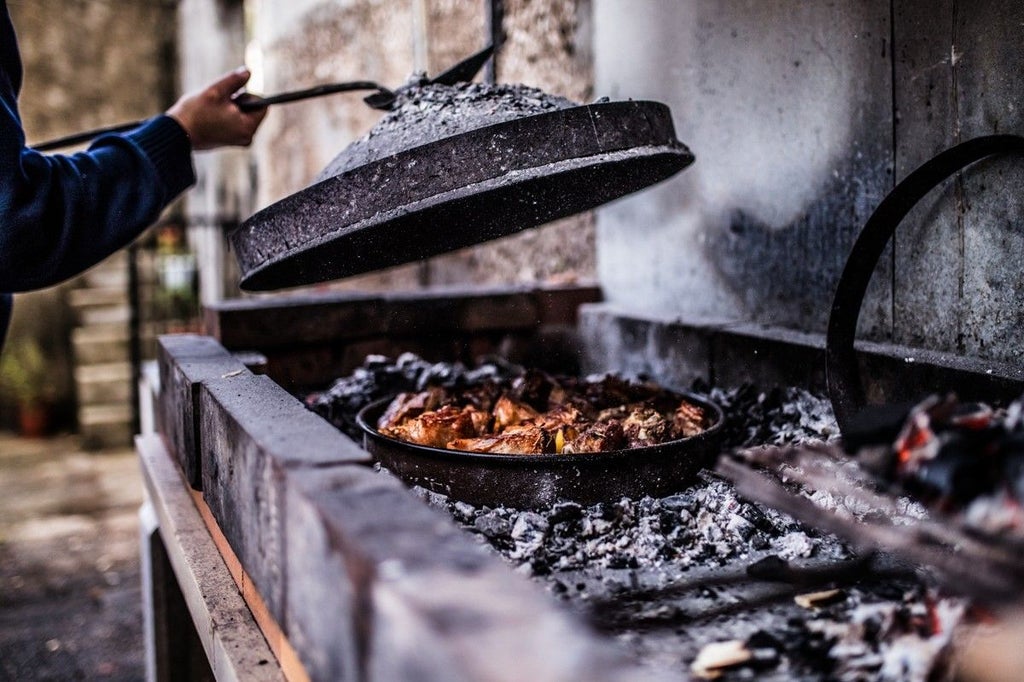 Chef in traditional Croatian attire demonstrates cooking local specialties in a rustic stone kitchen with copper cookware and herbs