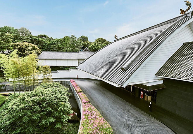 Modern hotel facade with sleek glass panels and illuminated signage, surrounded by lush greenery and featuring a grand entrance with valet service