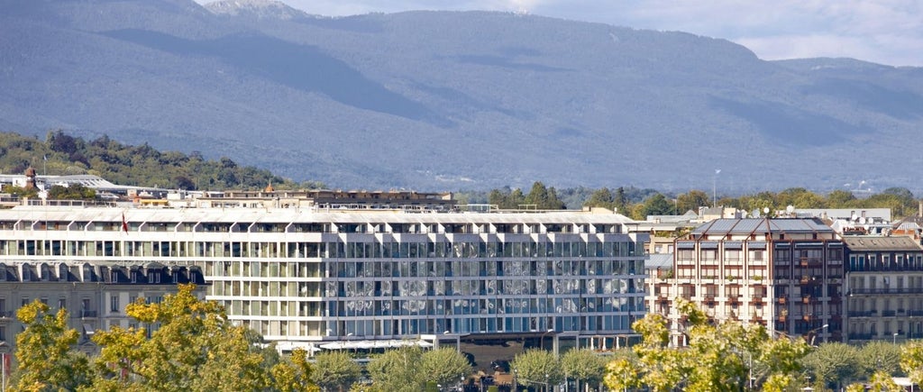 Opulent five-star Fairmont Grand Hotel Geneva overlooking Lake Geneva, with elegant stone facade and waterfront promenade at dusk