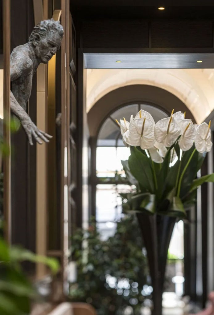 Elegant Italian hotel exterior with Art Deco-inspired columns, bronze doors, and stone facade illuminated by warm lighting at dusk