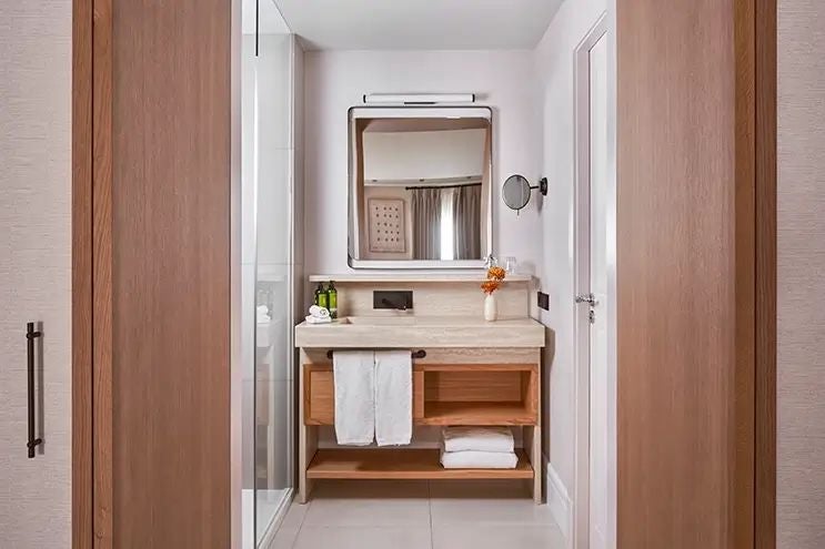 Elegant Spanish hotel room with warm wooden accents, plush white bedding, and rustic stone wall in a sophisticated, minimalist design