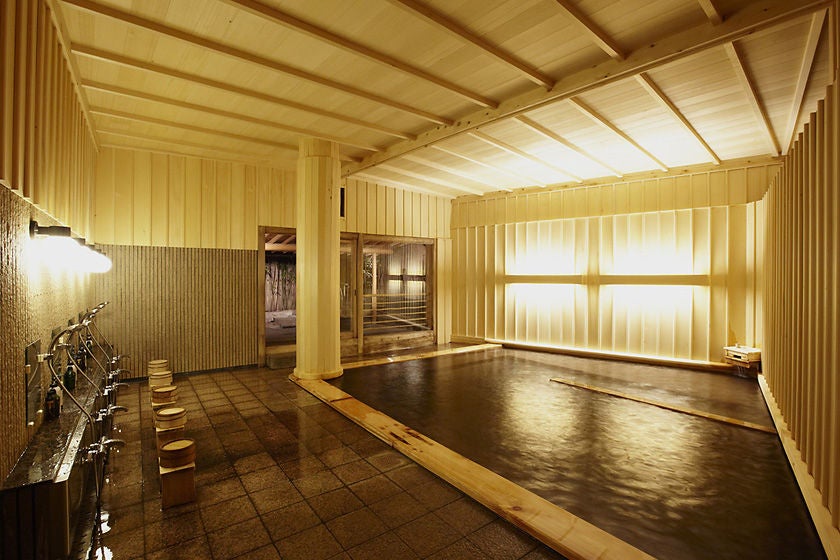 Traditional Japanese ryokan with elegant wooden architecture, featuring a tranquil outdoor onsen bath surrounded by bamboo and stone lanterns