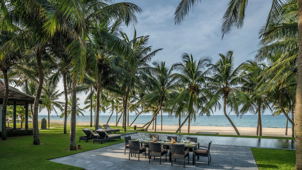 Beachfront villa with infinity pool overlooking pristine Vietnamese coastline, surrounded by palm trees and tropical gardens at dusk