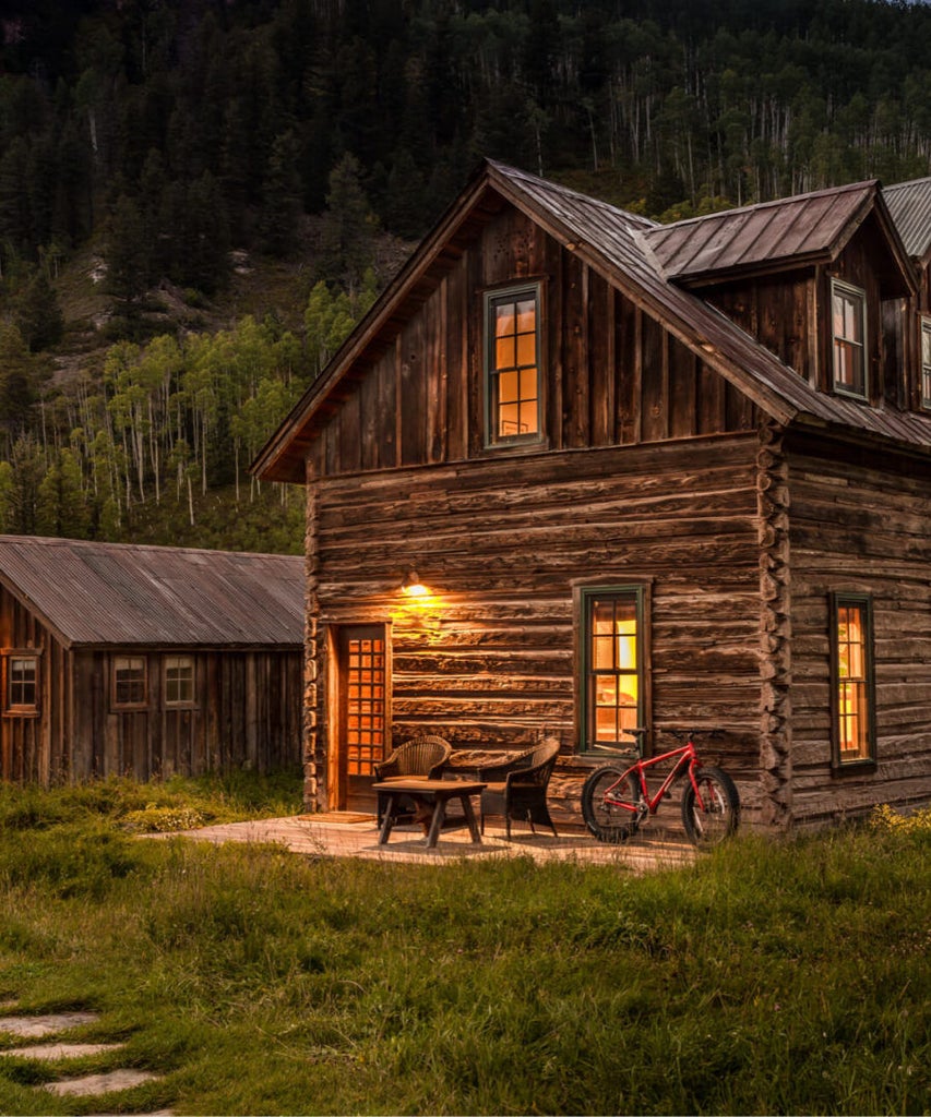 Snow-covered rustic luxury cabins nestled in Colorado mountains, with steaming natural hot springs and panoramic wilderness views