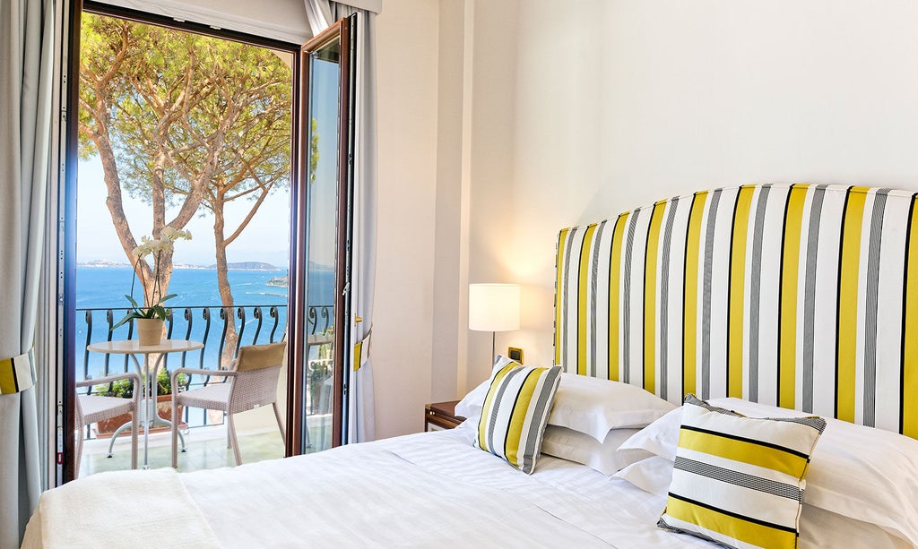 Elegant hotel room with panoramic sea views, white furnishings, tiled floors, and a private balcony overlooking the Italian coast