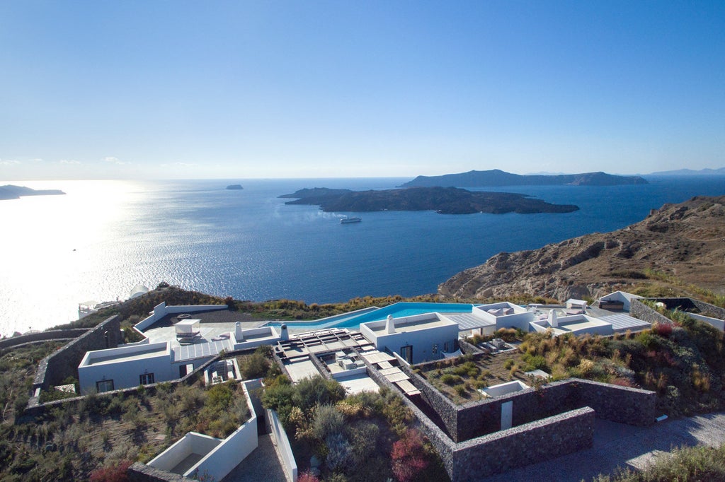 Luxury infinity pool with white sun loungers overlooking Santorini's caldera at sunset, framed by minimal Cycladic architecture