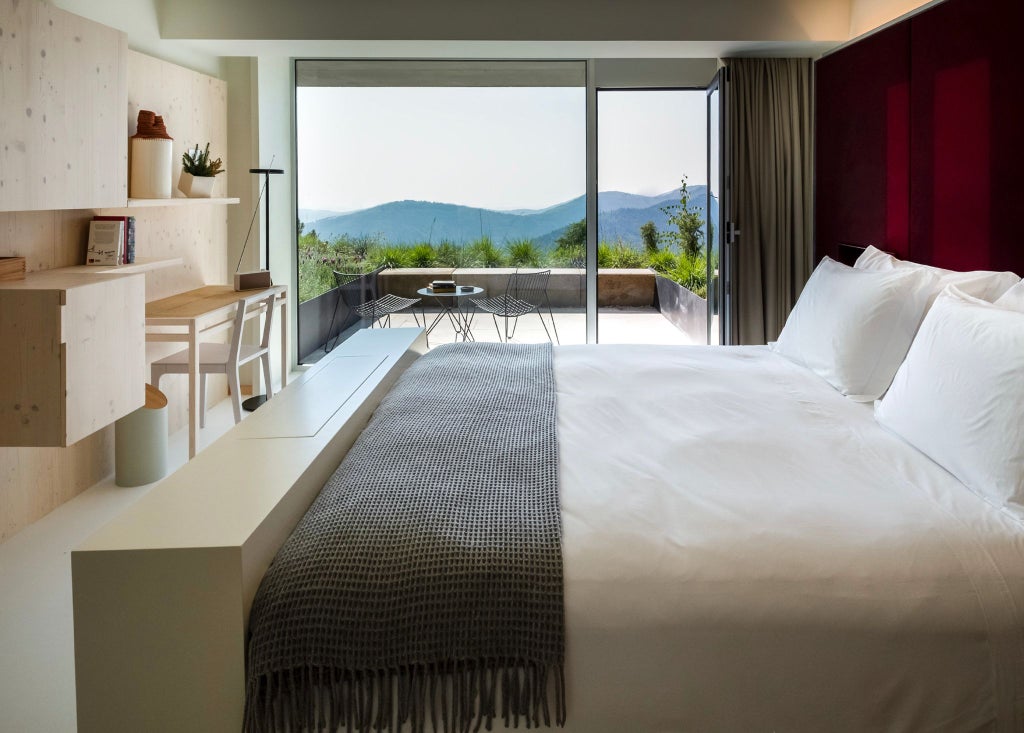 Modern, minimalist hotel room with floor-to-ceiling windows overlooking stunning Portuguese mountain landscape, featuring sleek wooden furniture and elegant design aesthetic