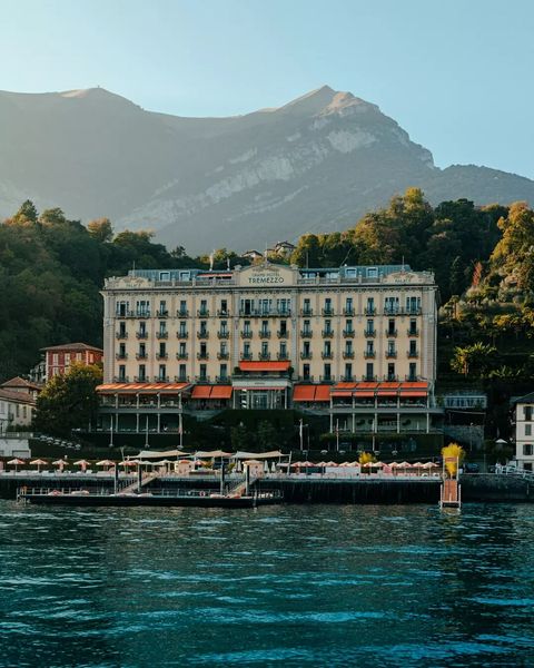 Five-star lakefront hotel with art nouveau facade, red awnings, and terraced gardens overlooking Lake Como's sparkling blue waters