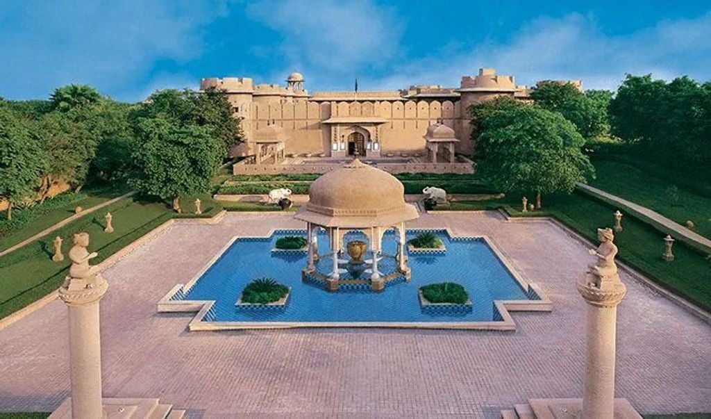 Elegant pool area at luxury hotel with domed sandstone pavilions, manicured gardens, and traditional Rajasthani architecture at sunset