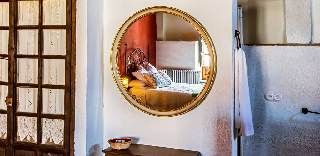 Elegant Spanish country hotel room with whitewashed walls, rustic wooden beams, plush king bed, and panoramic window overlooking serene landscape