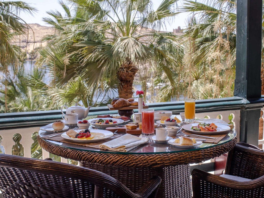 Elegant pink-hued historic luxury hotel nestled on the Nile River's banks, showcasing Moorish architecture with palm trees and colonial-era grandeur in Aswan, Egypt