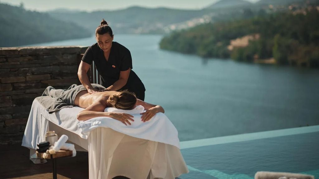 Luxury riverside hotel in Douro Valley with infinity pool overlooking terraced vineyards and winding river against mountain backdrop