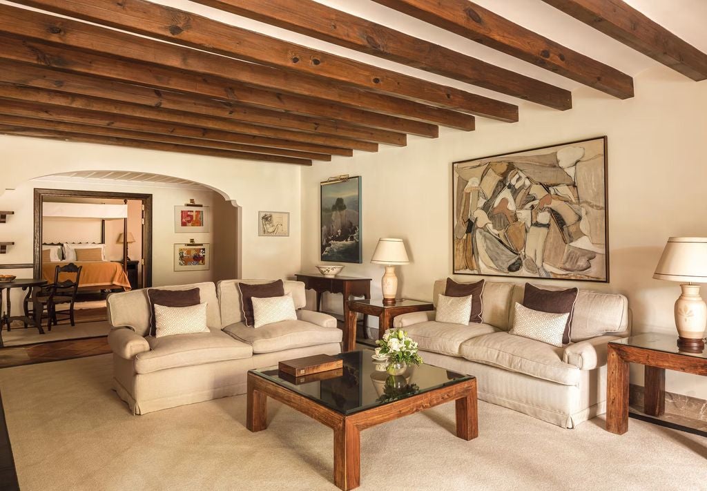 Elegant hotel suite with rustic stone walls, exposed beams, and French doors opening to a private terrace with mountain views in Mallorca.