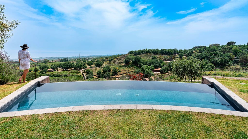 Elegant estate suite terrace overlooking volcanic landscape with infinity pool, lush greenery, and Mount Etna in background at Monaci delle Terre Nere