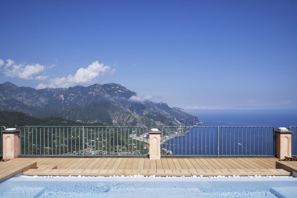 Elegant pink palatial hotel perched on Amalfi Coast cliffside, featuring ornate balconies and terraced gardens with Mediterranean views