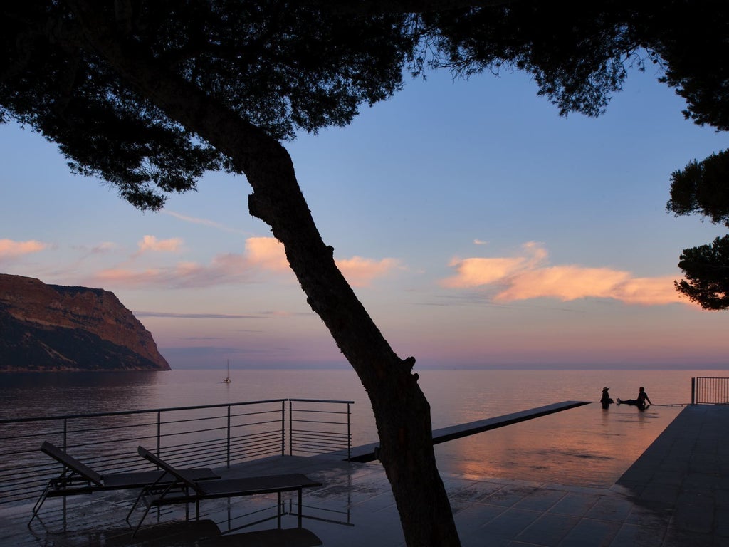 Elegant French Riviera hotel with white stone facade, panoramic Mediterranean views, palm trees, and opulent terraced gardens overlooking the sea