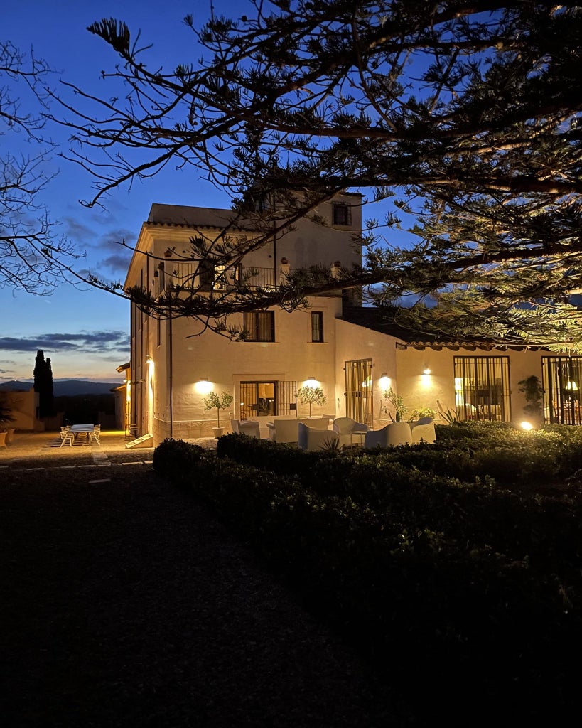 Elegant Sicilian boutique hotel Scenset nestled among olive groves, featuring sun-drenched stone walls and a serene Mediterranean landscape at golden hour