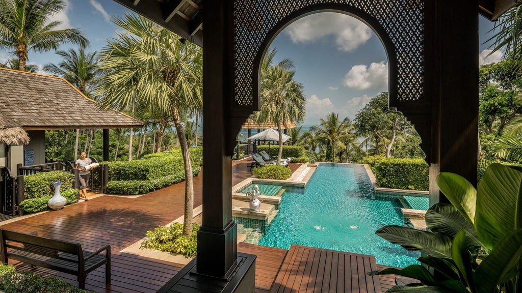 Palm-fringed infinity pool overlooking turquoise Gulf of Thailand, with luxurious ocean-view villas nestled into tropical hillside landscape