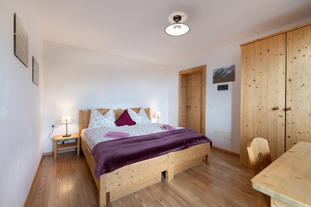 Luxurious wooden-paneled suite featuring a king bed with white linens, rustic timber beams, and panoramic mountain views through large windows