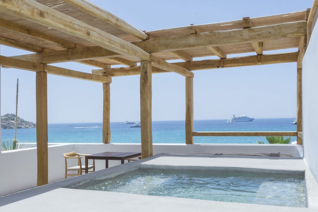 Luxurious white-themed deluxe hotel room with private jacuzzi, expansive Aegean Sea views, and minimalist elegant Mykonos design aesthetic