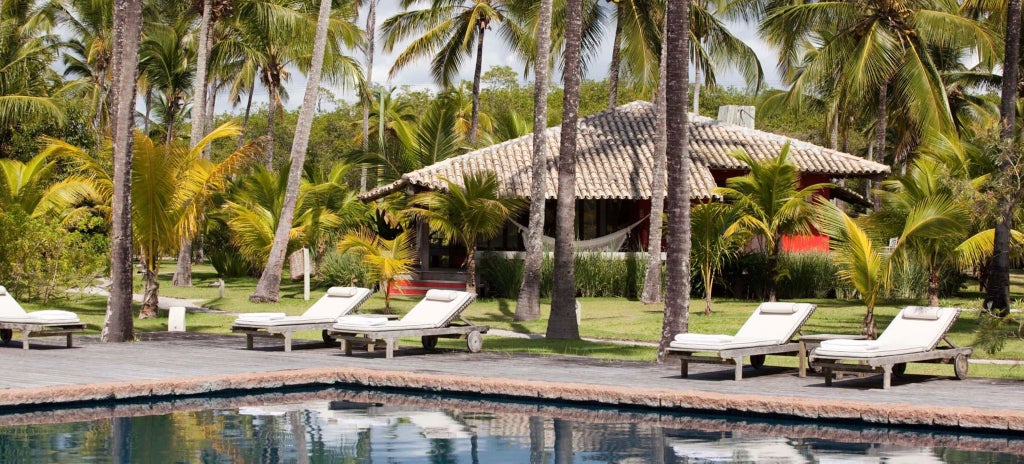 Luxurious Brazilian beach resort bungalow suite with elegant wooden furniture, soft white linens, and tropical forest view through large windows