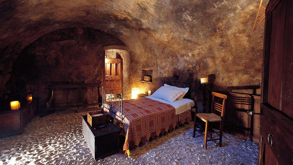 Rustic Italian hotel room with stone walls, wooden furniture, and soft lighting, showcasing minimalist luxury in a restored historic setting