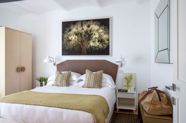 Rustic-chic Italian hotel room with warm terracotta walls, elegant wooden furnishings, plush white bedding, and soft natural light streaming through artisan windows