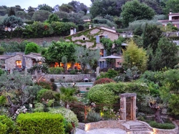 Elegant French boutique hotel nestled in lush greenery, featuring stone facade, manicured gardens, and soft morning light in scenic countryside setting