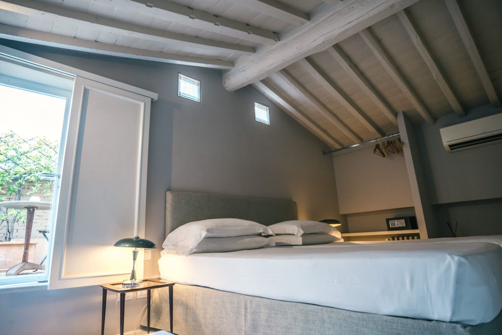 Minimalist junior suite in scenset hotel with exposed wooden beams, muted earth tones, modern furnishings, and large windows overlooking Italian landscape